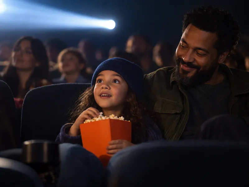 Une enfant et son père dans une salle de cinéma, un cornet de pop-corn à la main